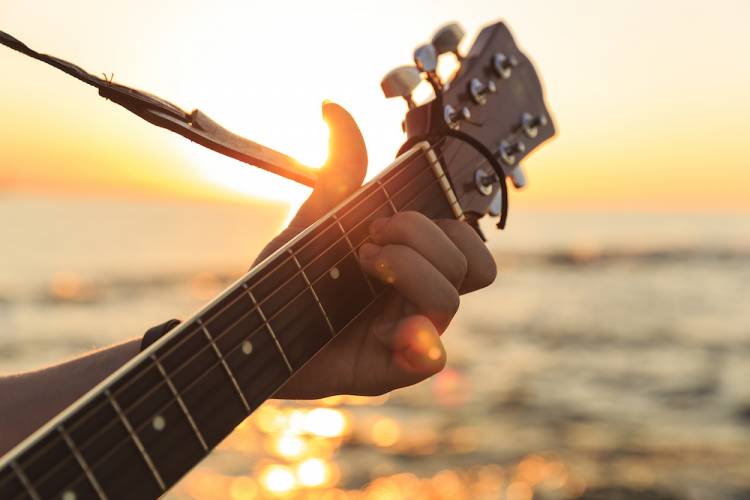 person playing a guitar with water visible in the background on a sunny day